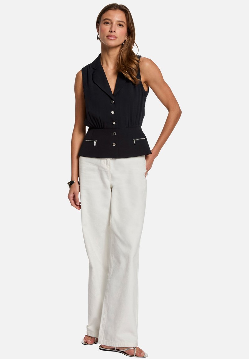 Blouse sans manches noire avec un décolleté en V, boutons sur le devant et taille peplum ; associé à un pantalon blanc à jambes larges et des sandales à lanières.