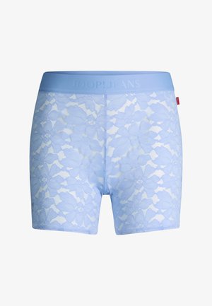 Nahaufnahme einer Person, die hellblaue florale Spitzen-Shorts mit breitem Bund und einem kleinen roten Etikett an der Seite trägt.