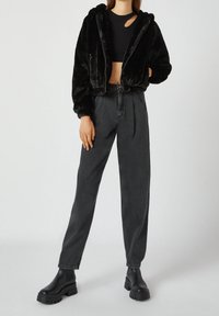 Veste courte en fausse fourrure noire avec capuche, associée à un pantalon en denim gris foncé taille haute et des bottines noires épaisses.