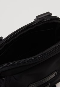 Borsa in tessuto nero con apertura con zip, caratterizzata da una texture liscia e una piccola tasca interna. Accentuata da un'etichetta in pelle.