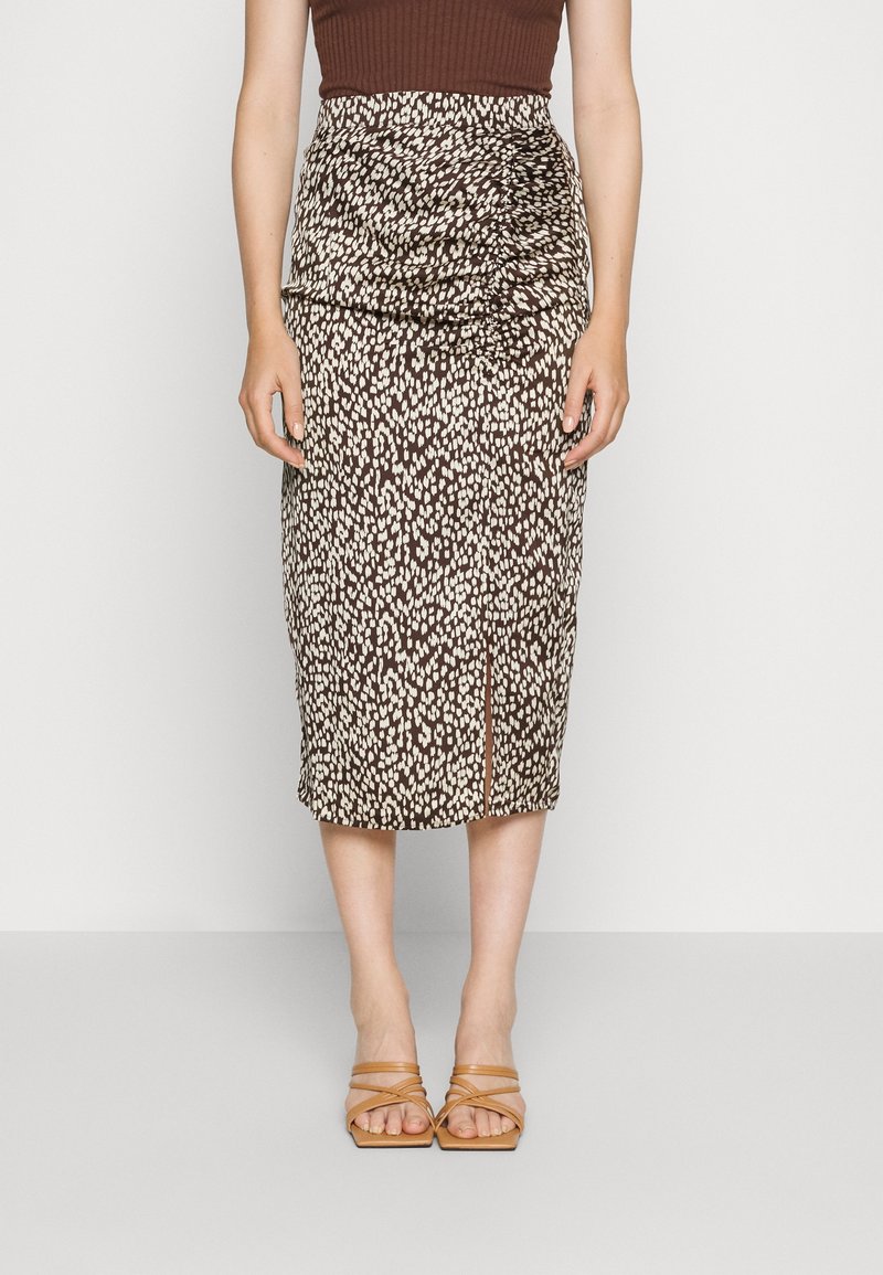 Femme portant une jupe midi marron et blanche à taches avec une fente à l'avant, associée à des sandales à talons ouvertes à brides couleur tan.