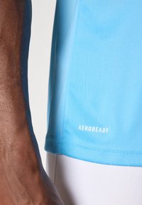 Camisola desportiva azul AeroReady com textura suave, apresentando linhas verticais e um logótipo branco na bainha inferior.