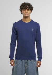 Navy blue sweatshirt with long sleeves, crew neck, and white anchor logo on the chest. Made from soft fabric with ribbed cuffs and hem.