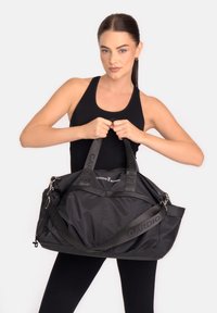 Fekete sporttáska dupla fogóval és levehető vállpánttal; sima, tartós anyagból készült, és feltűnő "CARDIO BUNNY" márkajelzéssel.