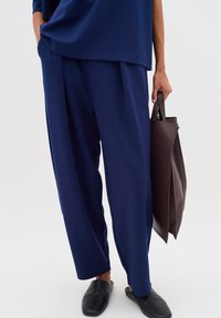 Navy blue wide-leg pants in a soft fabric, paired with black slip-on shoes and a dark brown leather tote bag, with a minimalistic design.