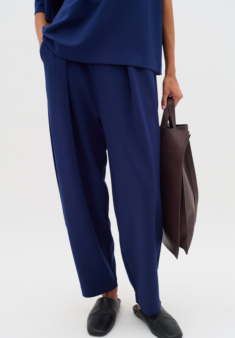 Navy blue wide-leg pants in a soft fabric, paired with black slip-on shoes and a dark brown leather tote bag, with a minimalistic design.
