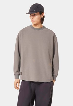 Gray textured long-sleeve shirt with a crew neckline. Features ribbed fabric and matching cuffs. Worn with a dark cap, highlighting casual style.