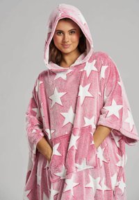 Rosa huva poncho gjort av mjukt, texturerat tyg, med stora vita stjärnmönster. Inkluderar en framficka och vida ärmar.