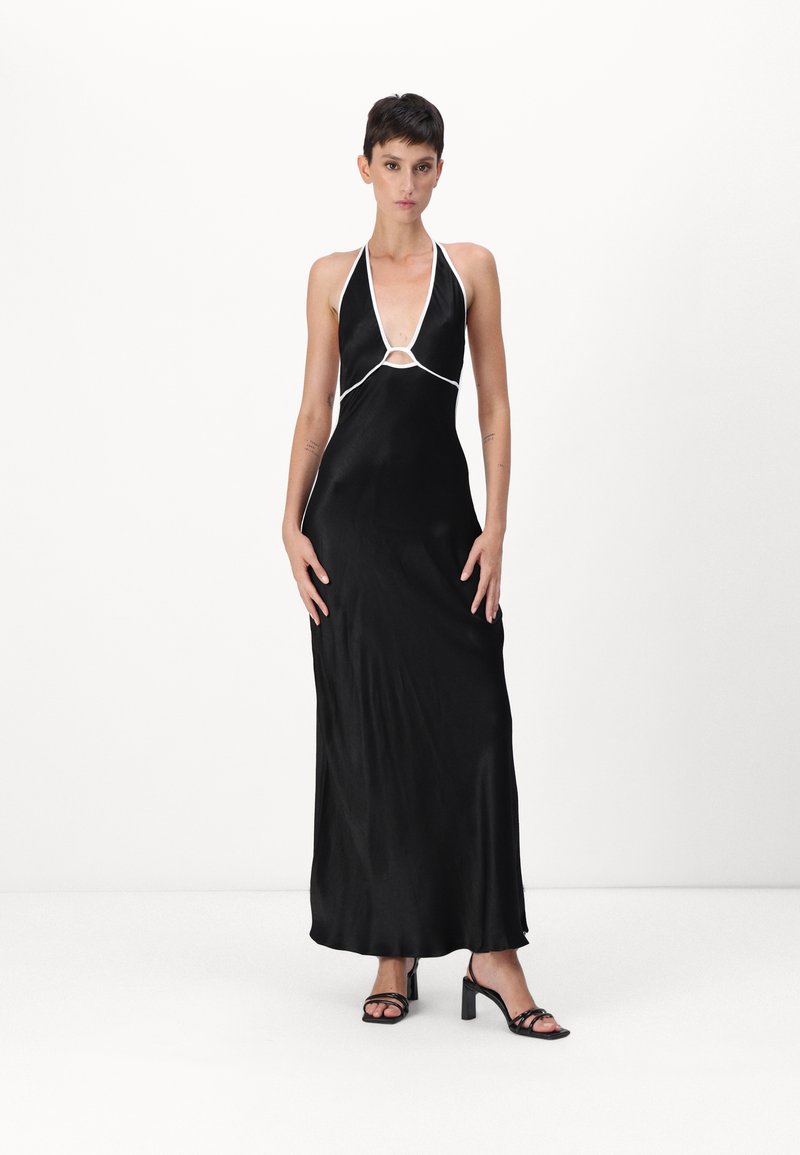 Black satin halter dress with white accents, featuring a deep V-neck, keyhole cutout, and a flowing silhouette. Worn with black heeled sandals.
