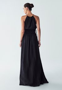Black halter maxi dress with a smocked waist. The fabric appears smooth with a slight sheen, featuring a relaxed fit and flowing silhouette.