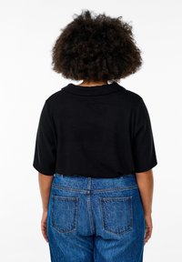 Svart kortärmad topp med krage, kombinerad med midjehöga blå denimjeans med bakfickor och en något lös passform.