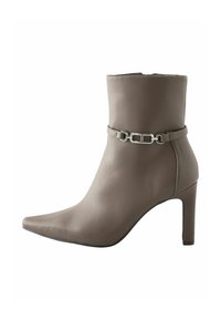 Bottine en cuir taupe avec un bout pointu, un talon haut et un détail décoratif en chaîne argentée autour de la cheville. Texture lisse, design minimaliste.