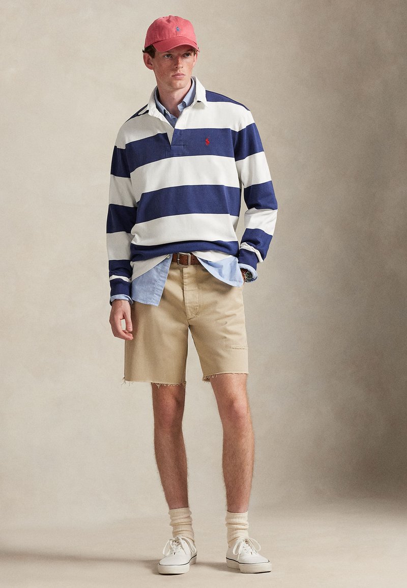 Navy and white striped long-sleeve polo, light blue shirt underneath, beige shorts, pink cap, white sneakers, and cream socks with a ribbed texture.
