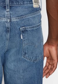 Ljusblå denimjeans med en bakficka som har ett signatur sömmönster. Tagg synlig vid midjan. Strukturerad tygfinish.