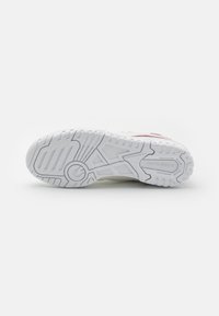 Semelle de chaussure blanche New Balance avec motif de bande de roulement texturé et marquage, vue de dessous sur fond uni.
