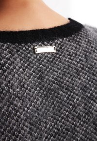 Pull gris en tricot avec un motif texturé, doté d'un col noir et d'une étiquette en métal argenté à l'arrière près de l'encolure.