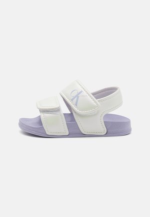 Bele sintetike bele na dveh prilagodljivih Velcro trakih, vijolična podplata in odtisnjen logotip na zgornjem traku.