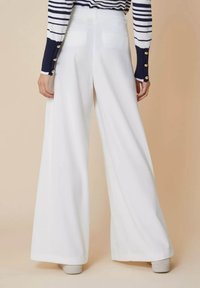 Wijdvallende witte broek met een gladde textuur, voorzien van achterzakken en een hoge taille. De gestylede outfit omvat een navyblauw en wit gestreept shirt.