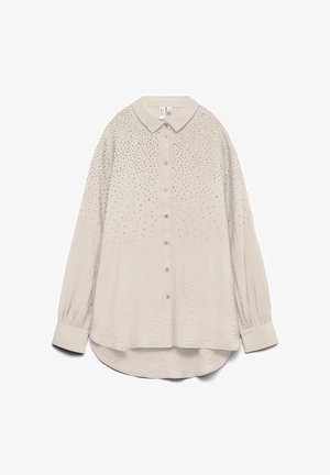 Lysebeige skjorte med knapper og en spredt krave, prydet med en gradient af små sorte nitter på den øverste halvdel og lange, let puffede ærmer.