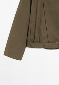 Giacca verde oliva con una texture liscia, tasca laterale, orlo elasticizzato e cintura regolabile con più fori per la personalizzazione della vestibilità.