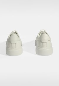 White leather sneakers with rounded backs, textured surfaces, and matching laces, featuring a low-profile rubber sole and stitching details.