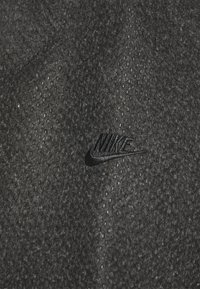 Tela negra texturizada con pequeños puntos en relieve. Presenta un logo de Nike negro bordado en la superficie. Textura suave y lisa en general.