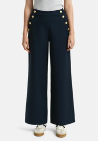 Pantalon large bleu marine à taille haute, doté de boutons dorés en accents sur le côté et d'un tissu lisse et texturé.