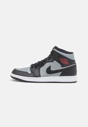 Schwarz-grauer High-Top Nike Air Jordan Sneaker mit rotem Logo, schwarzem Swoosh, weißer Zwischensohle und schwarzer Außensohle auf weißem Hintergrund.