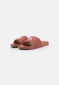 Sandali slide di colore terracotta con tomaia in tessuto. Presentano un design con punta aperta, suola piatta e un evidente dettaglio logo bianco.