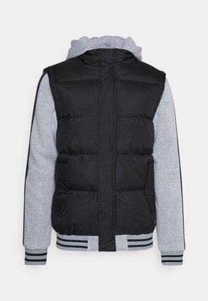 Sort puffervæst med grå sweatshirtærmer, ribbede manchetter og bund, og med sidelommer og hætte. Den strukturerede stofkontrast giver variation i stilarterne.