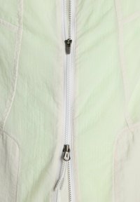 Gros plan d'un tissu vert pâle avec une double fermeture éclair blanche, montrant deux curseurs en métal sur un matériau texturé.