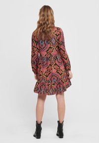 Robe longue à manches longues imprimée avec une jupe évasée, présentant un motif paisley multicolore sur fond noir. Bottes noires à la cheville.