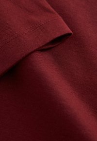 Nahaufnahme von gefaltetem kastanienbraunem Stoff mit feiner Strickstruktur und doppelt genähtem Saum auf weichem Baumwollmaterial.