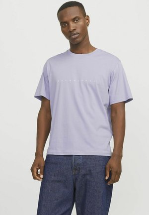 Camiseta de algodón lila de manga corta, con cuello redondo y el logo blanco "JACK&JONES" impreso en el pecho. Combinada con jeans oscuros.
