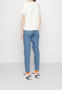 Camiseta blanca de manga corta, combinada con jeans azul claro con bolsillos laterales. Zapatillas blancas con detalles en negro y rojo, y calcetines naranjas.
