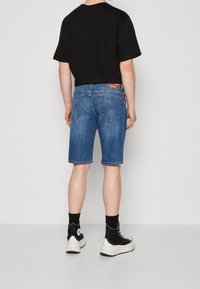 Shorts de mezclilla en azul claro con un corte regular, con bolsillos traseros y una etiqueta de marca. Combinados con una camiseta negra de manga corta.