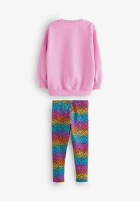 Felpa rosa a maniche lunghe con polsini a coste sopra leggins multicolori con un motivo ondulato di blu, viola, arancione e rosa.