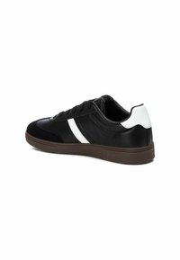 Sneaker neri con una combinazione di suede e pelle, dotati di una striscia bianca e suola in gomma marrone. Texture liscia con accenti a contrasto.