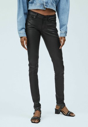 Widok od pasa w dół osoby noszącej czarne, dopasowane skórzane spodnie, jasnoniebieską, krótką kurtkę dżinsową oraz czarne, ćwiekowane sandały na obcasie.