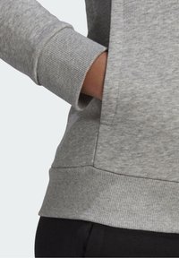 Šedá mikina má hladkou texturu, žebrované manžety a boční kapsu. Lem je také žebrovaný, což poskytuje strukturované padnutí.