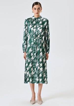 Robe longue à boutons en motif géométrique vert et blanc. Dispose d'une taille ceinturée, de manches longues et d'un col. Texture de tissu lisse.