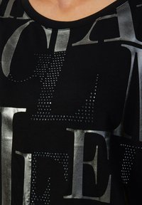 Schwarzes T-Shirt mit großen metallischen grauen Buchstaben und Strassverzierungen, rundem Ausschnitt und weichem Stoffgefühl.