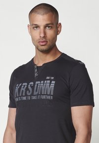 Juoda trumpa rankovė t-shirt, pagaminta iš medvilnės, su henley tipo iškirpte, pilka grafika tekstu ir mygtukais ant peties.