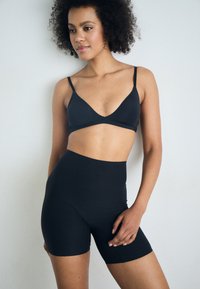 Black seamless bra with a triangular cut and thin straps paired with high-waisted black bike shorts. Smooth texture, form-fitting design.