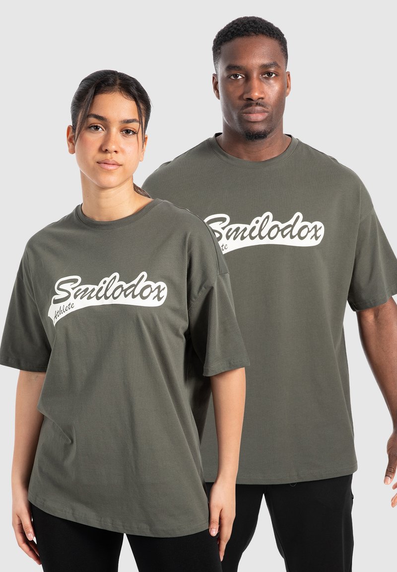 Camisetas de algodón verdes con un corte relajado, que presentan un logo blanco de "Smilodox" y el texto "Athlete" en el frente. Mangas cortas, diseño simple.