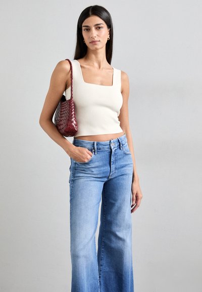 Svijetlo bež crop top s kvadratnim izrezom, visokotirali plavi razvučeni traperice i tamnocrvena pletena torba s remenom za rame. Glatka tekstura.