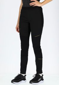 Black athletic pants with a slim fit, featuring textured panels, gold accents, and elastic waistband, paired with black sneakers.