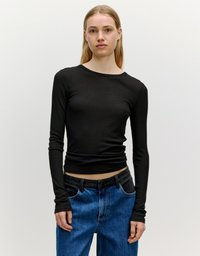 Zwarte langärmmode met een aansluitende pasvorm, ribbelstructuur, ronde halslijn en duimgaten in de manchetten, gecombineerd met hoog-waist blauwe denim jeans.