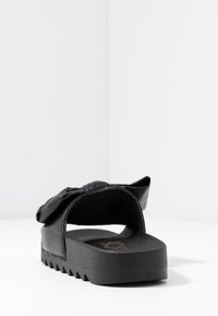 Black slide sandal with textured platform sole and padded upper featuring a large, soft bow detail, shown from rear angle.