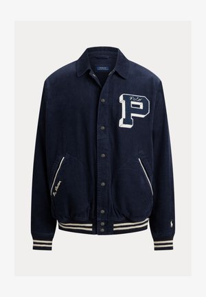 Casaco de veludo cotelê azul-marinho com fecho de botão, grande emblema branco com a letra "P" no peito, punhos e barra listrados, duas bolsos frontais com acabamento branco.
